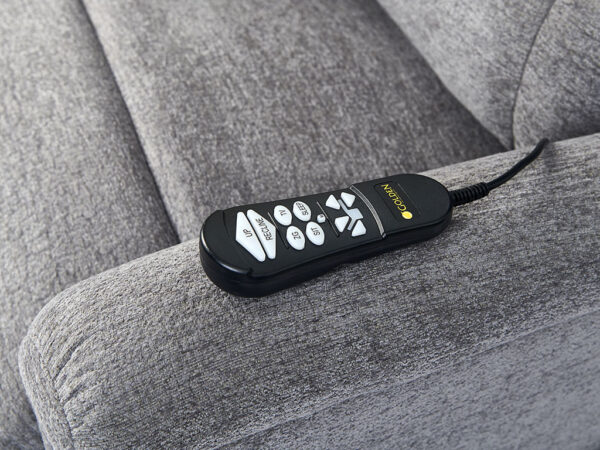 A Comforter with MaxiComfort Large remote control featuring multiple buttons is resting on a gray upholstered couch.