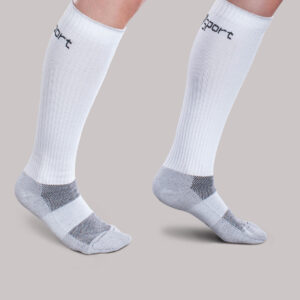 Two legs wearing Core-Sport by Therafirm white knee-high athletic socks with grey accents, standing on one leg against a plain grey background.